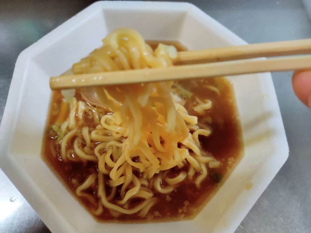 「日清豚ラ王 ヤサイ、アブラ、ニンニク」の麺を持ち上げた写真。